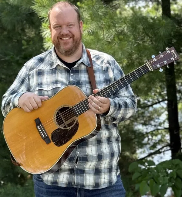 Justin Smith smiling with a dreadnought acoustic guitar outdoors