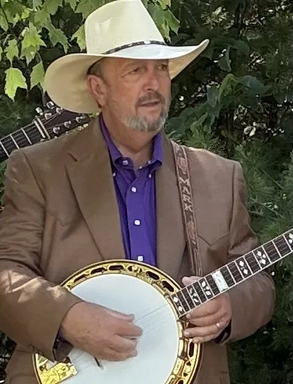 Mark Krider in a white hat and tan jacket playing banjo outdoors